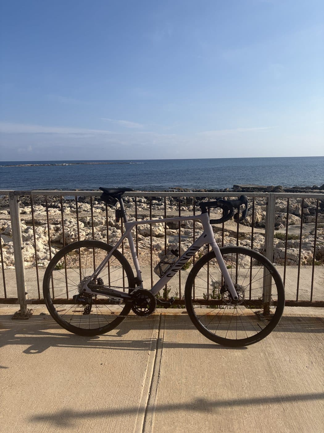 My road bike leaning against a rusty seafront railing, rocky shore and open sea behind it